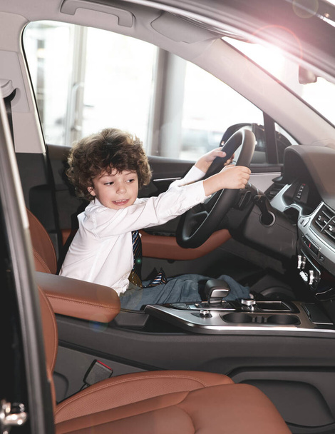 Діти спостерігають і тестують нову машину в дилерстві. Маленький хлопчик сидить на водійському сидінні, автомобільній кабіні. Маленький хлопчик тримає руки на кермі, посміхаючись
. - Фото, зображення