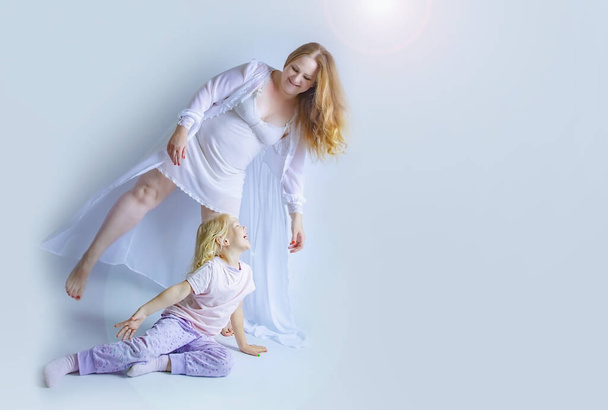Overweight or pregnant mother with her daughter in pajamas have a fun. Healthy lifestyle concept. Children and adults on bright background. Happy family together. Copy space - Foto, immagini