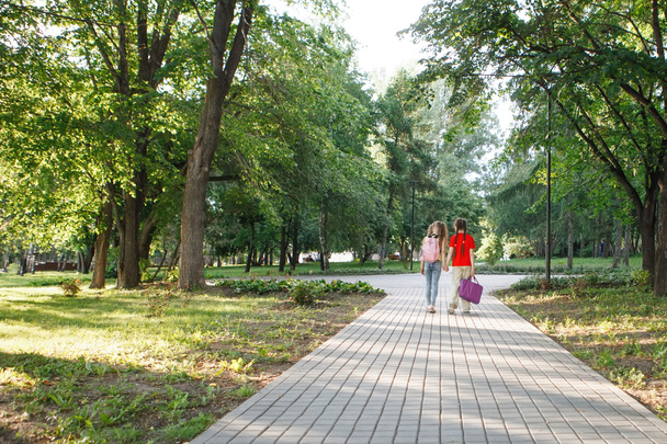 Δύο έφηβες κοπέλες περπατούν στο πεζοδρόμιο στο πάρκο.. - Φωτογραφία, εικόνα