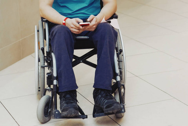 Un hombre vistiendo una camiseta azul en una silla de ruedas mirando en un smarp
 - Foto, Imagen