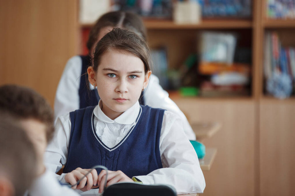 Χαριτωμένο μαθήτρια κάθεται στο γραφείο της σε μια σχολική τάξη. - Φωτογραφία, εικόνα
