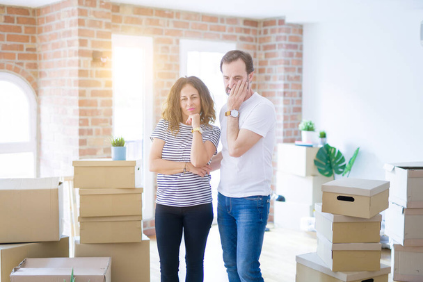 Middle age senior couple moving to a new home with boxes around thinking looking tired and bored with depression problems with crossed arms. - Photo, Image