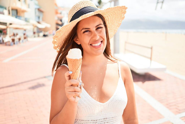 Nuori kaunis nainen syö jäätelöä kartio rannalla aurinkoisena kesäpäivänä lomilla
 - Valokuva, kuva