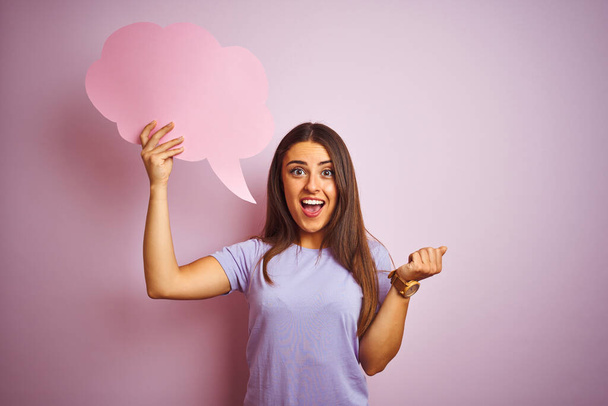 Young beautiful woman holding cloud speech bubble over isolated pink background screaming proud and celebrating victory and success very excited, cheering emotion - Foto, immagini