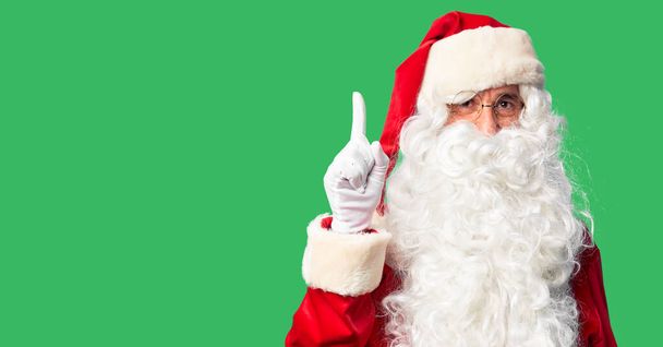 Красивый мужчина средних лет в костюме Санта-Клауса и с бородой, показывая пальцем на успешную идею. Взволнован и счастлив. Номер один
. - Фото, изображение