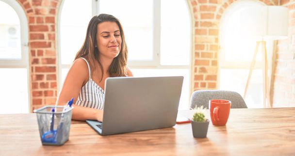 Молода красива бізнес-леді працює за допомогою ноутбука вдома або в офісі, посміхаючись позитивно
 - Фото, зображення