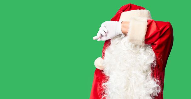 Middelbare leeftijd knappe man in Santa Claus kostuum en baard staan te dekken ogen met arm, kijken ernstig en verdrietig. Zichteloos, verstoppertje en afwijzing - Foto, afbeelding
