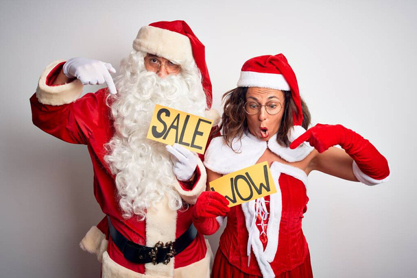 Pari yllään Santa puku tilalla wow ja myynti banneri yli eristetty valkoinen tausta Osoittaa alas sormilla näyttää mainosta, yllättynyt kasvot ja avoin suu
 - Valokuva, kuva