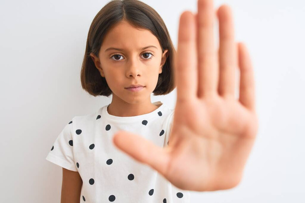 Mladý krásný dítě dívka na sobě ležérní tričko stojící nad izolovaným bílým pozadím s otevřenou rukou dělat stop sign s vážným a sebejistý výraz, obrana gesto - Fotografie, Obrázek