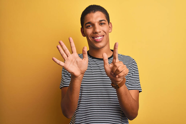 Nuori komea arabi mies yllään merivoimien raidallinen t-paita yli eristetty keltainen tausta osoittaa ylös sormet numero seitsemän hymyillen itsevarma ja onnellinen
. - Valokuva, kuva