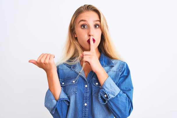 Young beautiful woman wearing casual denim shirt standing over isolated white background asking to be quiet with finger on lips pointing with hand to the side. Silence and secret concept. - Foto, Imagem