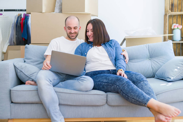 Jovem casal sentado no sofá em nova casa usando computador portátil
 - Foto, Imagem