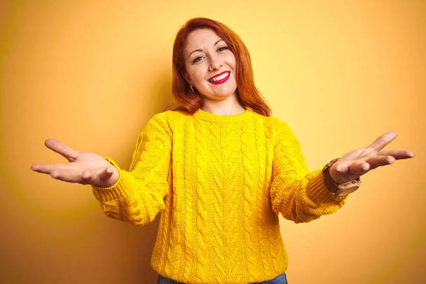 Belle rousse femme portant pull d'hiver debout sur fond jaune isolé souriant joyeuse offrant des mains donnant assistance et acceptation
. - Photo, image