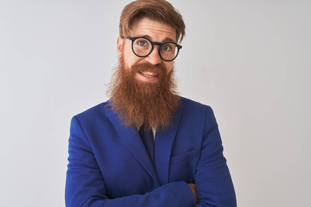 Jonge Redhead Ierse zakenman dragen pak en bril over geïsoleerde witte achtergrond gelukkig gezicht glimlachend met gekruiste armen kijken naar de camera. Positieve persoon. - Foto, afbeelding