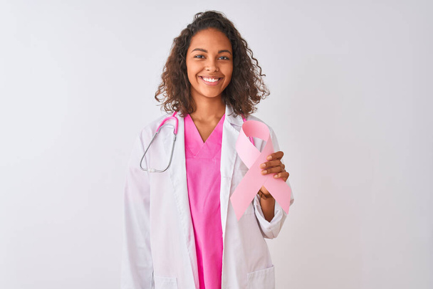 Młoda brazylijska lekarka trzymająca wstążkę nowotworową na odizolowanym białym tle ze szczęśliwą twarzą stojącą i uśmiechniętą z ufnym uśmiechem pokazującym zęby - Zdjęcie, obraz