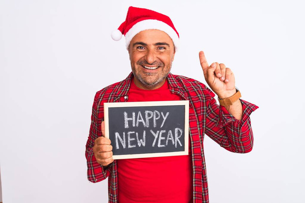 Человек в рождественской шляпе, держащий доску на изолированном белом фоне, удивленный идеей или вопросом, указывая пальцем со счастливым лицом, номер один
 - Фото, изображение