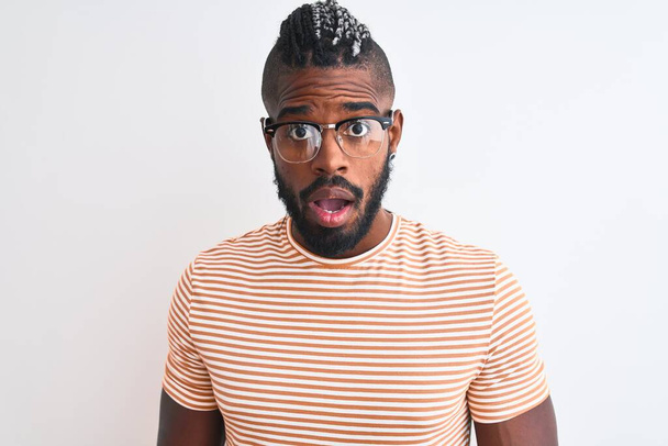 Hombre afroamericano vistiendo camiseta a rayas y gafas sobre fondo blanco aislado asustado y sorprendido con expresión sorpresa, miedo y cara excitada
. - Foto, imagen