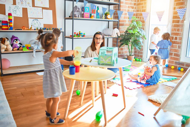 Красивий вчитель і група малюків грають навколо багатьох іграшок в дитячому саду
 - Фото, зображення