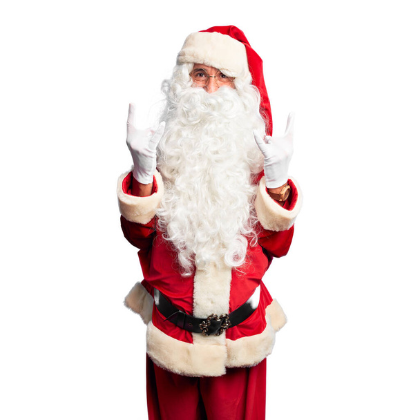 Keski-ikäinen komea mies yllään Joulupukin puku ja parta seisoo huutaen hullu ilme tekee rock symboli kädet ylhäällä. Musiikkitähti. Raskas musiikki käsite
. - Valokuva, kuva