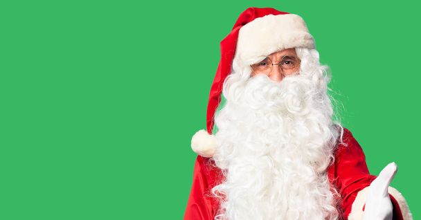 Pohledný muž středního věku v kostýmu Santa Clause a s vousy stojí a přátelsky se usmívá a nabízí pozdrav a přivítání. Úspěšná práce. - Fotografie, Obrázek
