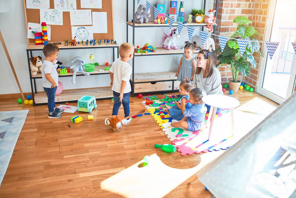 Beautiful teacher and group of toddlers playing around lots of toys at kindergarten - Foto, Bild