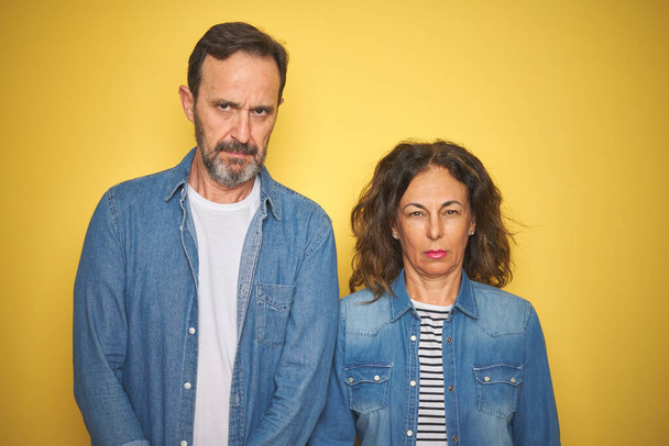 Beautiful middle age couple together wearing denim shirt over isolated yellow background skeptic and nervous, frowning upset because of problem. Negative person. - Photo, Image