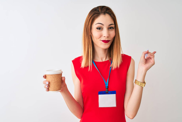 pelirroja mujer de negocios con tarjeta de identificación beber taza de café sobre fondo blanco aislado muy feliz señalando con la mano y el dedo a un lado
 - Foto, Imagen