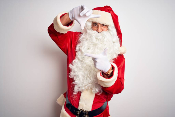 Middle age handsome man wearing Santa costume standing over isolated white background smiling making frame with hands and fingers with happy face. Creativity and photography concept. - Photo, Image