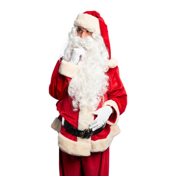 Middelbare leeftijd knappe man draagt Kerstman kostuum en baard staan met de hand op kin denken over vraag, penseelachtige uitdrukking. Lachend en attent gezicht. Twijfelachtig concept. - Foto, afbeelding