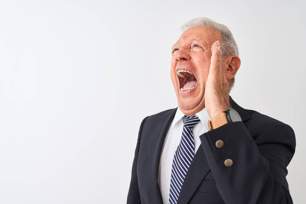 Senior grey-haired businessman wearing suit standing over isolated white background shouting and screaming loud to side with hand on mouth. Communication concept. - Fotoğraf, Görsel