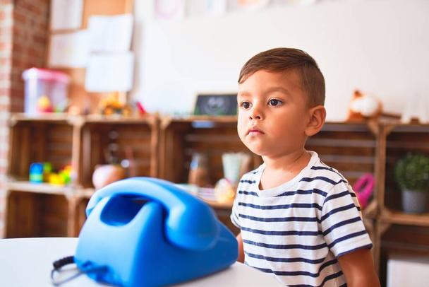 Красивый мальчик играет с винтажным синим телефоном в детском саду
 - Фото, изображение