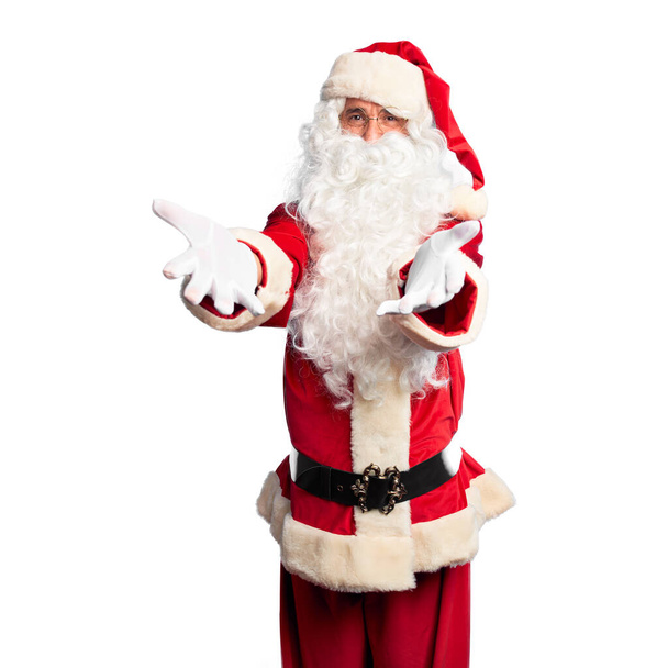 Middle age handsome man wearing Santa Claus costume and beard standing looking at the camera smiling with open arms for hug. Cheerful expression embracing happiness. - Photo, Image