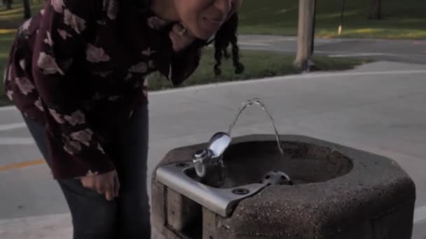 Кліп щасливої афроамериканської жінки, яка йде до публічного фонтану пиття і ковтає прохолодну освіжаючу воду, коли вона стримує своє волосся.. - Кадри, відео
