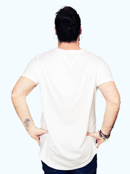 Jeune homme hipster aux cheveux longs et à la barbe portant un t-shirt blanc décontracté debout vers l'arrière, les bras sur le corps
 - Photo, image