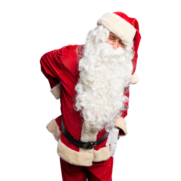 Красивый мужчина средних лет в костюме Санта-Клауса и с бородой стоя страдает от боли в спине, касаясь спины рукой, мышечной боли
 - Фото, изображение