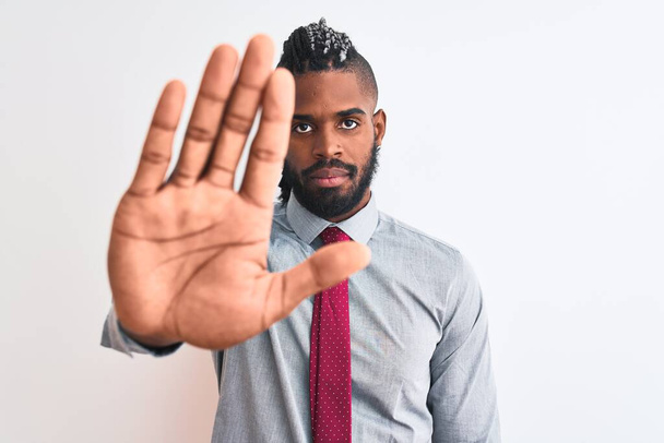 African american businessman with braids wearing tie standing over isolated white background doing stop sing with palm of the hand. Warning expression with negative and serious gesture on the face. - 写真・画像