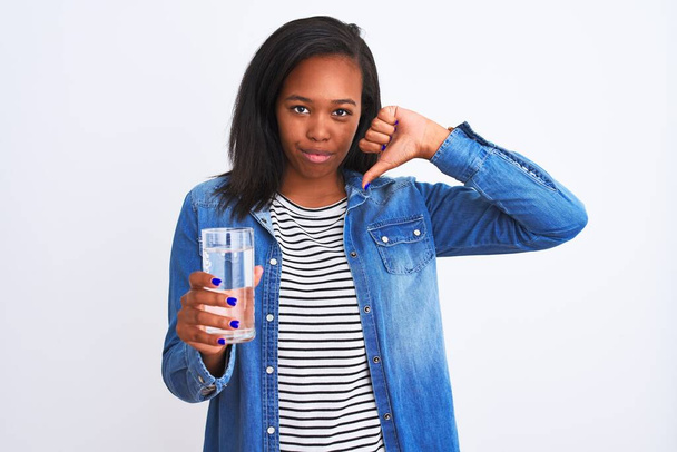 Giovane donna afroamericana bere un bicchiere di acqua dolce su sfondo isolato con viso arrabbiato, segno negativo mostrando antipatia con i pollici verso il basso, concetto di rifiuto
 - Foto, immagini