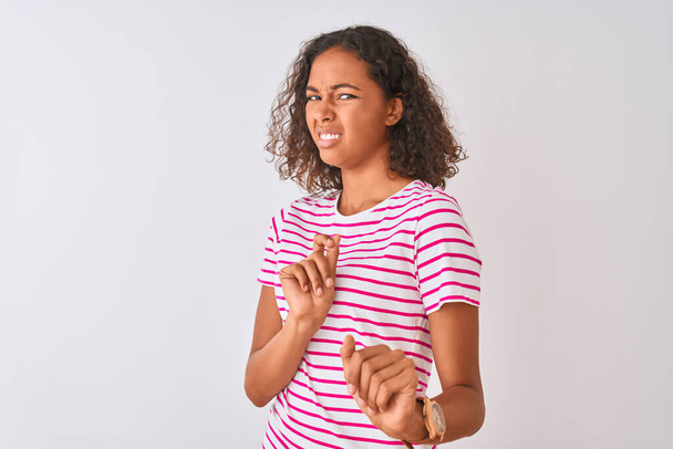 Young brazilian woman wearing pink striped t-shirt standing over isolated white background disgusted expression, displeased and fearful doing disgust face because aversion reaction. With hands raised. Annoying concept. - Foto, immagini