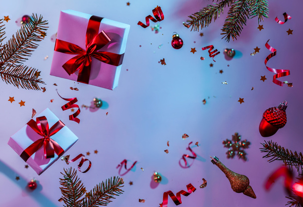 Kerstkaart gemaakt van vliegende decoraties, geschenkdozen, sparren takken, ballen, glitters en confetti op kleurrijke neon blauwe en paarse achtergrond. Kerstmis en nieuwjaarsvakantie, bokeh, lichten. Selectieve focus - Foto, afbeelding