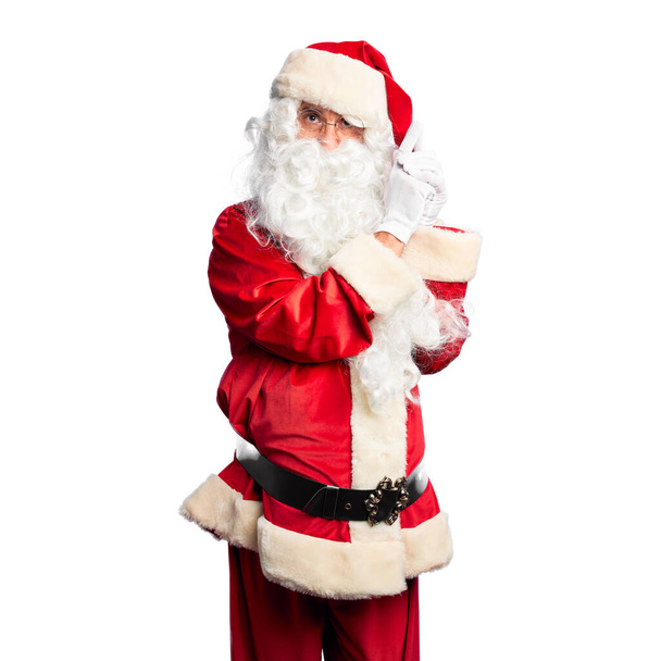 Middle age handsome man wearing Santa Claus costume and beard standing Holding symbolic gun with hand gesture, playing killing shooting weapons, angry face - Фото, изображение