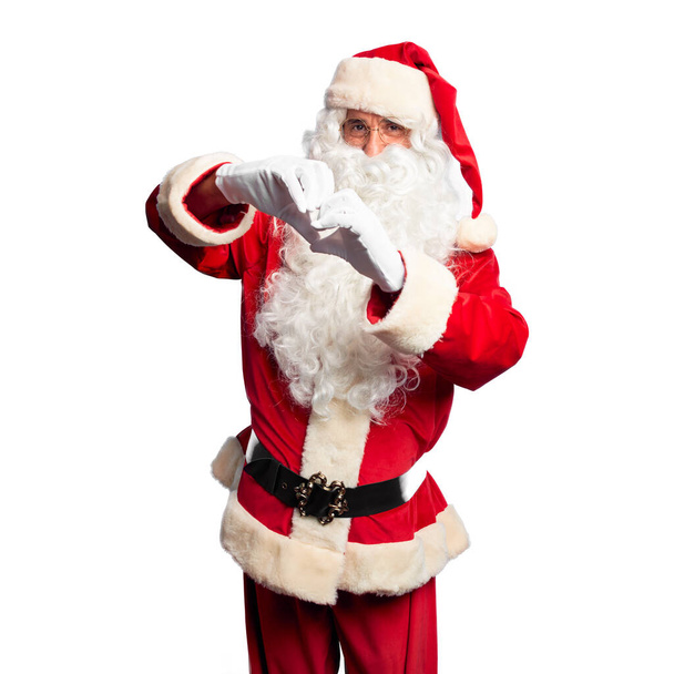 Przystojny mężczyzna w średnim wieku ubrany w kostium Świętego Mikołaja i brodę stojący uśmiechnięty w miłości robiąc ręcznie symbol serca. Romantyczna koncepcja. - Zdjęcie, obraz