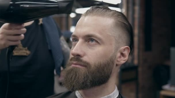 Young handsome bearded man at barbershop, shallow depth of field. Drying hair process - Imágenes, Vídeo
