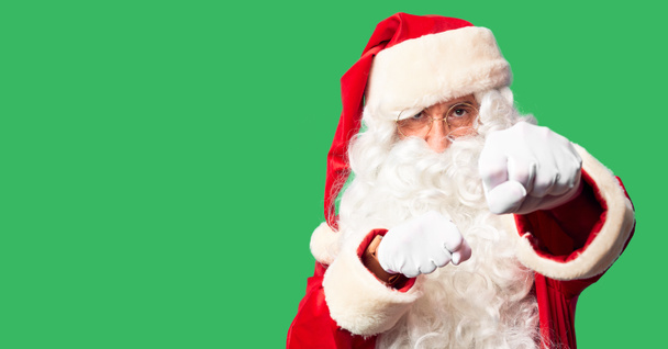 Homem bonito de meia idade vestindo traje de Papai Noel e barba de pé Punho de perfuração para lutar, ataque agressivo e irritado, ameaça e violência
 - Foto, Imagem