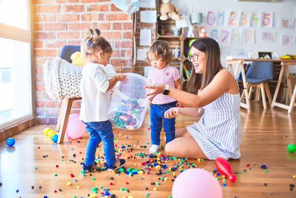 Joven hermosa maestra y niños pequeños jugando con bloques de construcción de juguete en el jardín de infantes
 - Foto, Imagen