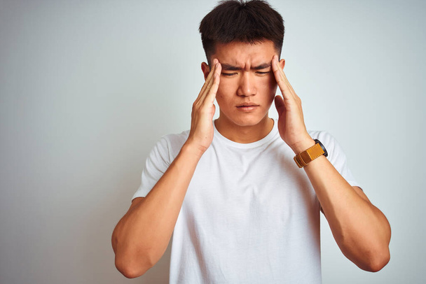 Młody Chińczyk w T-shircie stojący nad odizolowanym białym tłem z ręką na bólu głowy, ponieważ stres. Migrena cierpiąca. - Zdjęcie, obraz