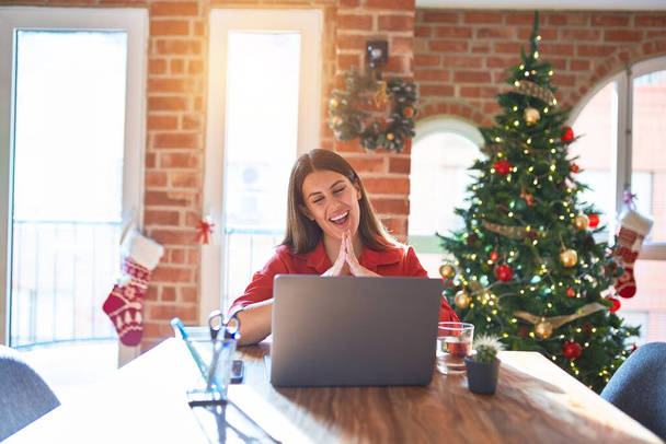 クリスマスツリーの周りの自宅でラップトップで作業テーブルに座っている美しい女性手と指がリラックスして陽気に笑顔を交わしました。成功と楽観的 - 写真・画像