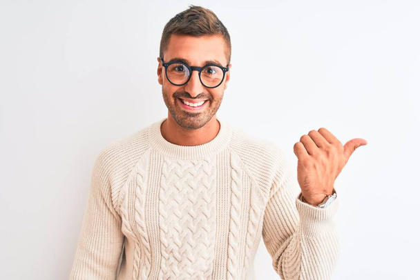 Young handsome man wearing glasses and winter sweater over isolated background pointing and showing with thumb up to the side with happy face smiling - Photo, Image