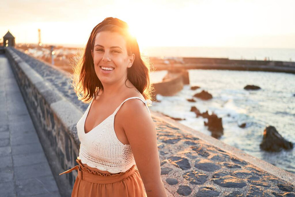 Beautiful young woman walking on beach promenade enjoying ocean view smiling happy on summer vacation - 写真・画像
