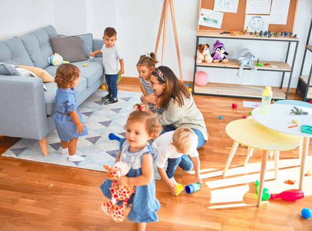 Beautiful teacher and group of toddlers playing around lots of toys at kindergarten - 写真・画像