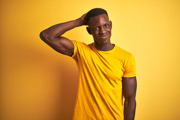 junger afrikanisch-amerikanischer Mann in lässigem T-Shirt, der vor isoliertem gelben Hintergrund steht, verwirrt und fragt sich über Fragen. Unsicher im Zweifel, mit der Hand auf dem Kopf denkend. Nachdenkliches Konzept. - Foto, Bild